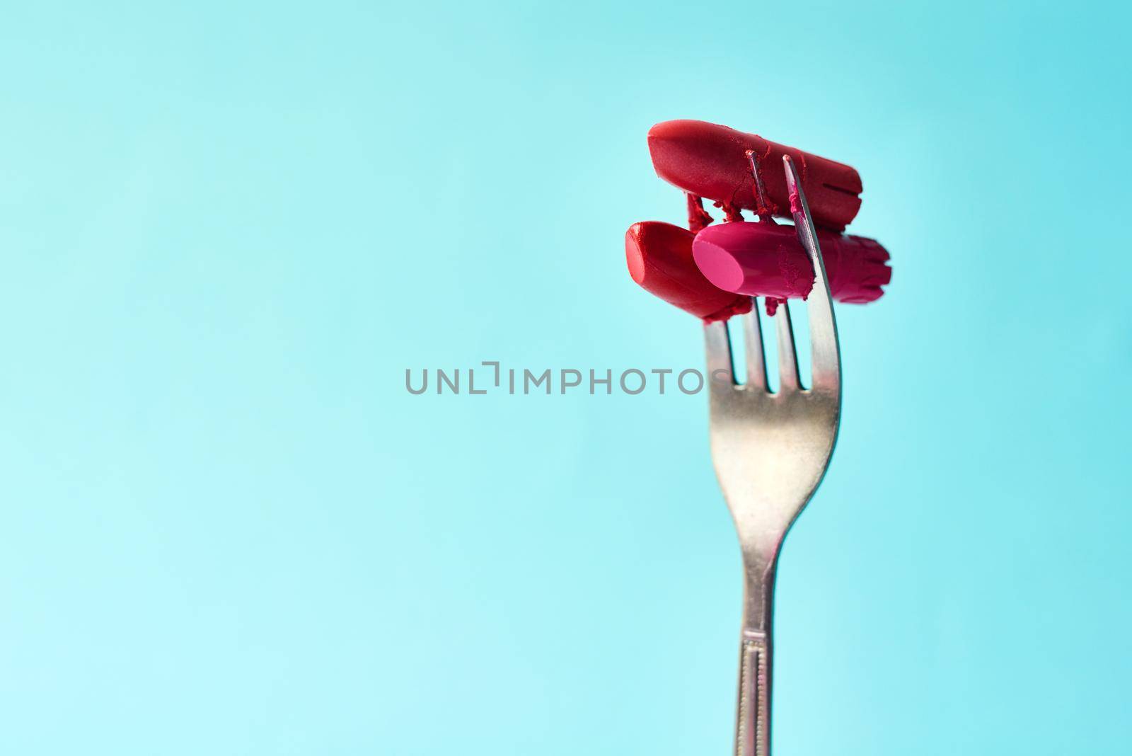 Cropped studio shot of lipstick on a fork against a turquoise background.