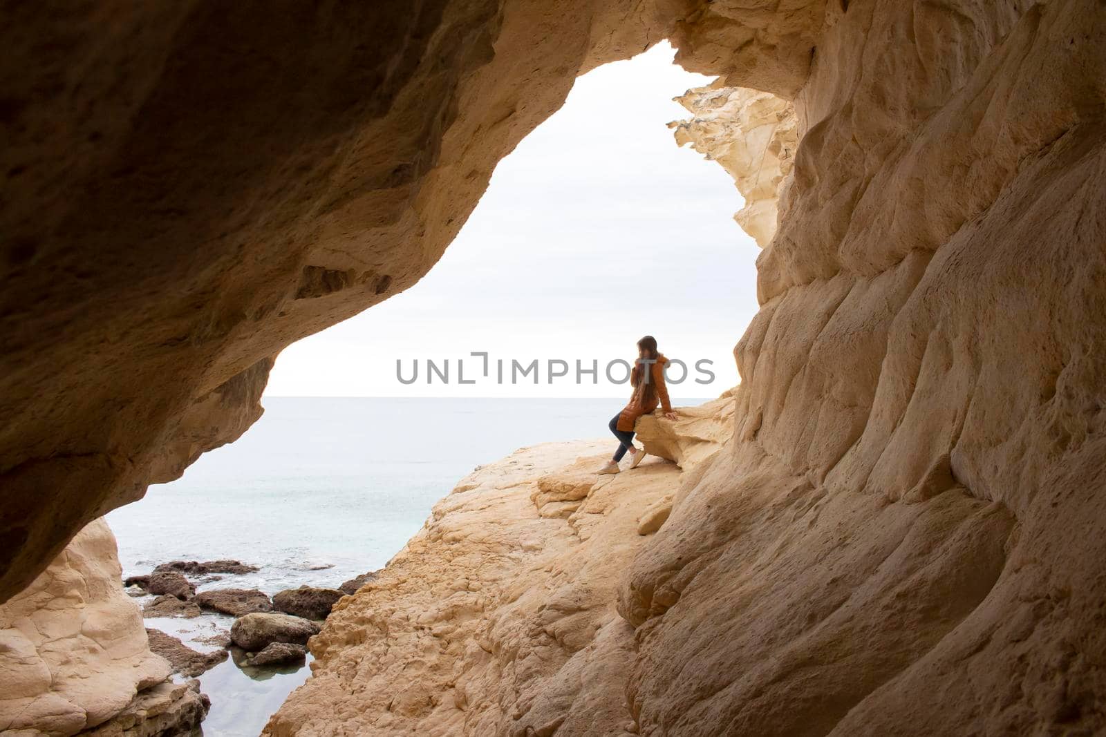 beautiful view in a bay from white cave to a sea with a girl sitting on a stone