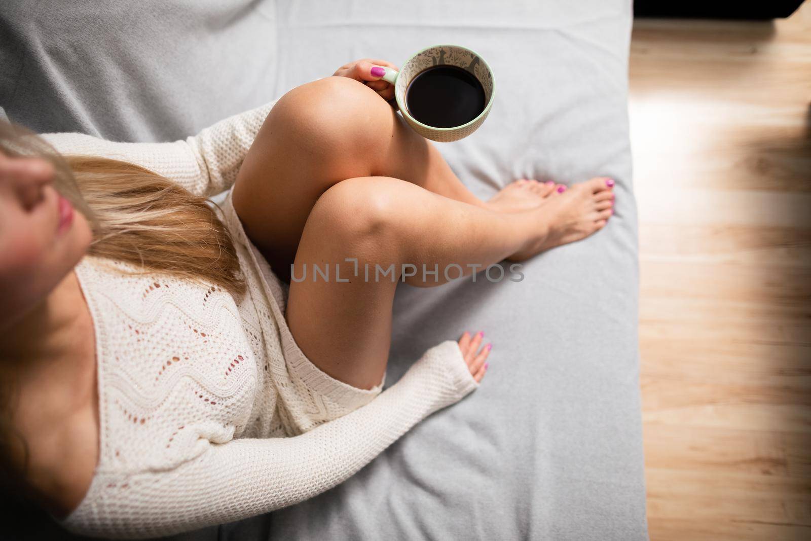 Cup of hot morning coffee held by woman. Sexy female legs with light skin complexion. Relaxing in the comfort of home.