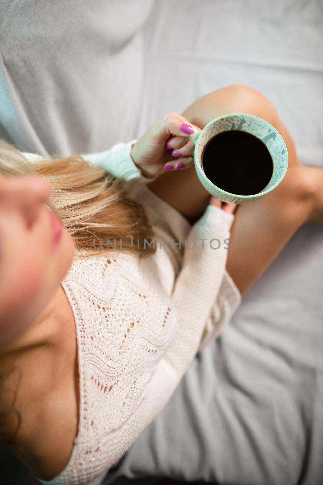 Cup of hot morning coffee held by woman. Sexy female legs with light skin complexion. Relaxing in the comfort of home.