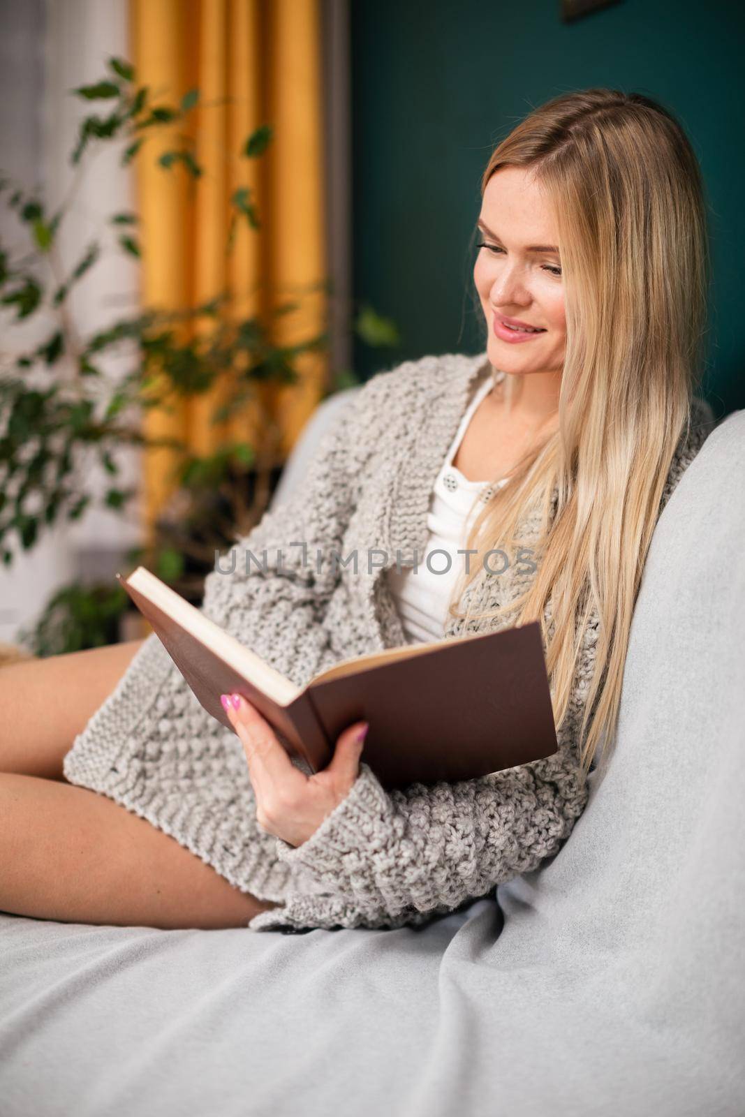 During leisure time at home, woman with shapely legs reads book while sitting on bed. A blonde woman while relaxing in the living room.