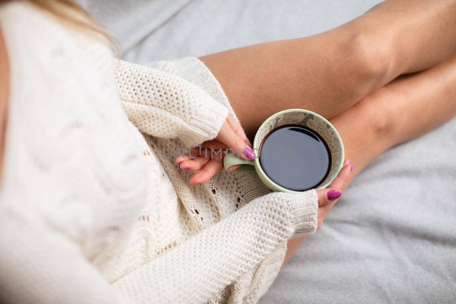 View from above as a woman with slim legs holds a porcelain cup with her morning coffee in her hands. Love coffee and relaxing in the comfort of home.