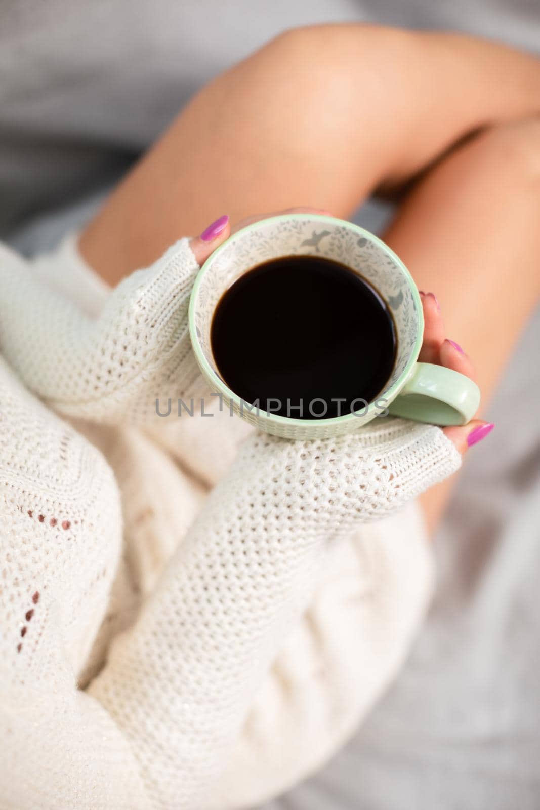 View from above as a woman in a cream sweater holds a delicately porcelain cup with hot coffee. Love coffee and relaxing in the comfort of your home.