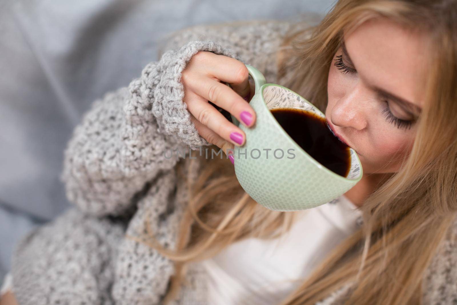 A young woman drinks hot coffee from a large cup in the morning. Close-up view. Aromatic coffee time while resting and relaxing.