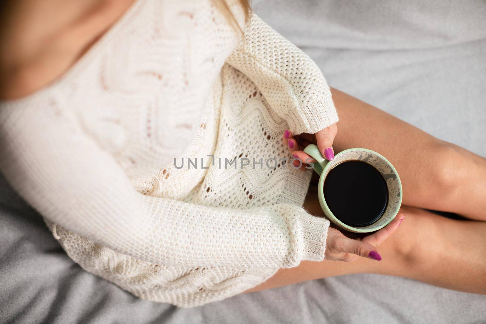 Top view of a woman holding a porcelain cup of coffee in her hands. Light complexion of the skin. Love for coffee and relaxation in the comfort of home.