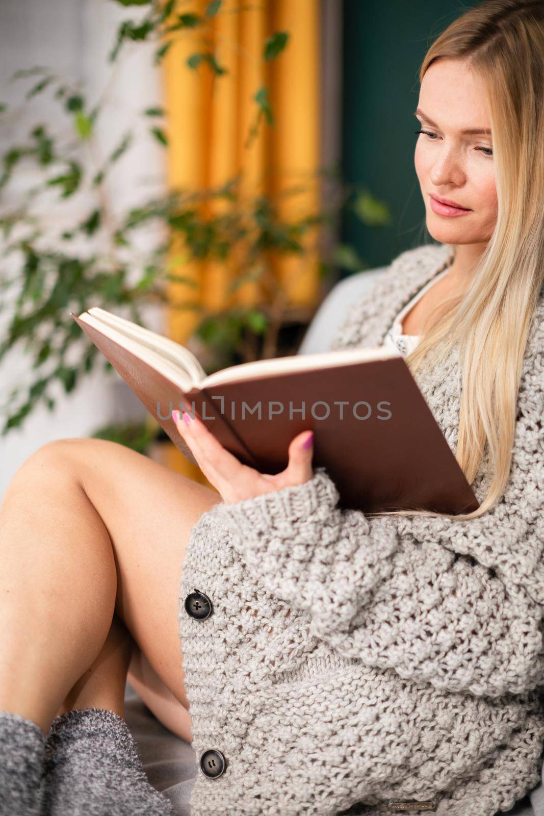 During leisure time at home, woman with shapely legs reads book while sitting on bed. A blonde woman while relaxing in the living room.