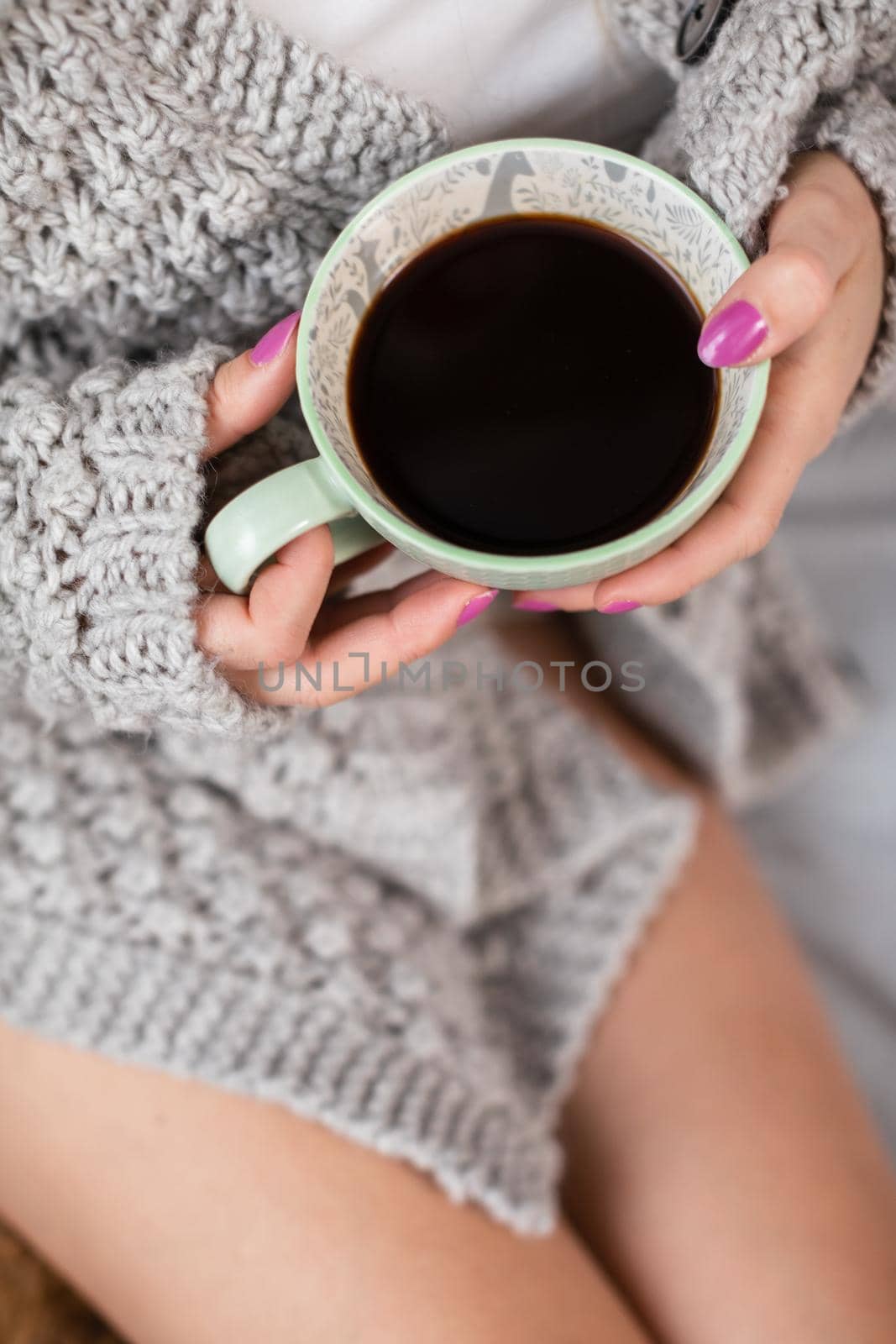 A cup of coffee in the gentle embrace of a woman's hands. The shapely female legs. Romantic time during relaxation.