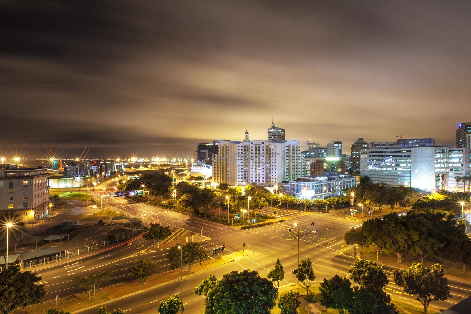 Scene of an inner city intersection with lights and clouds overhead.