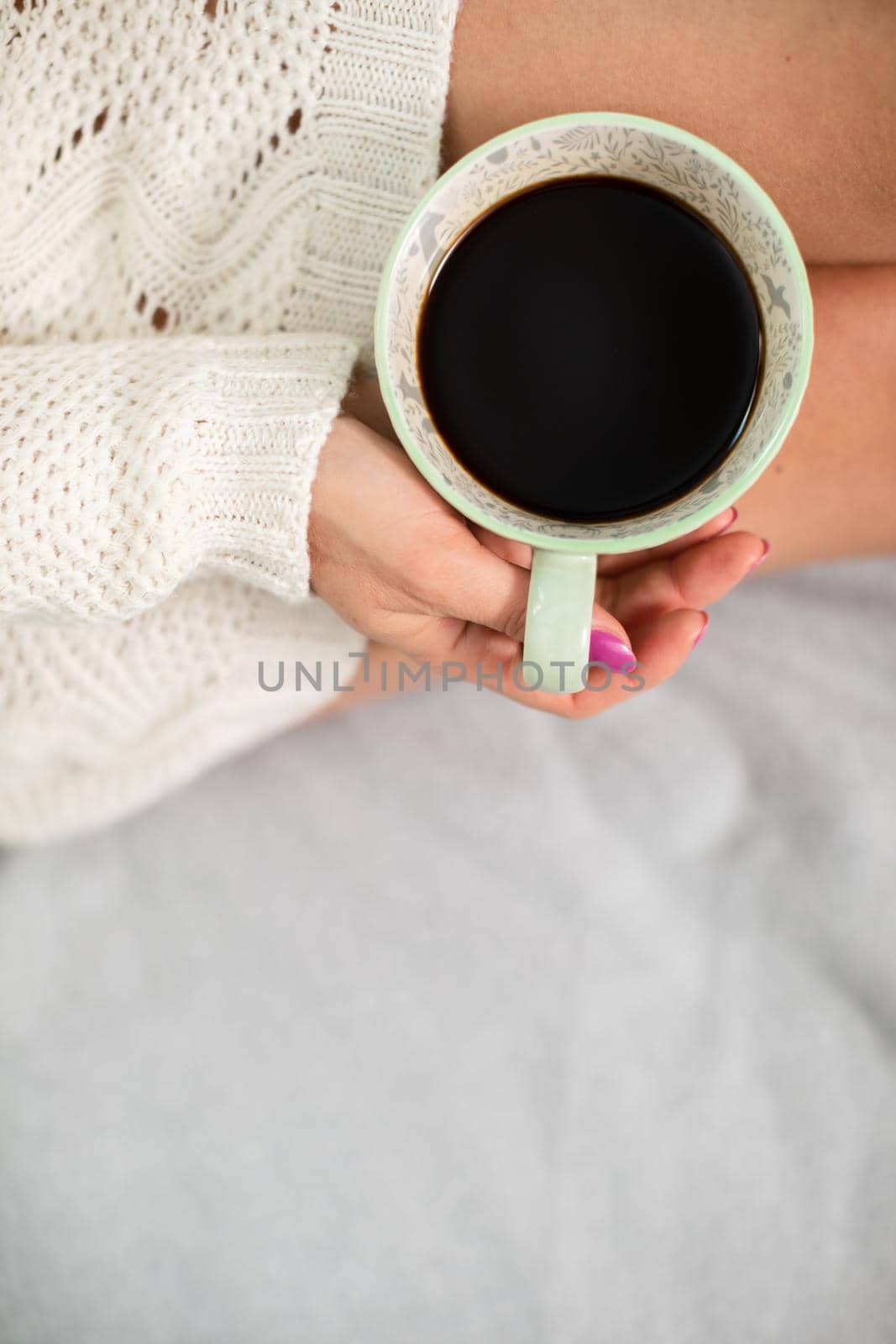 Slender female legs in grey wool socks. Porcelain cup with coffee in woman's hands. Relaxing in the comfort of home.