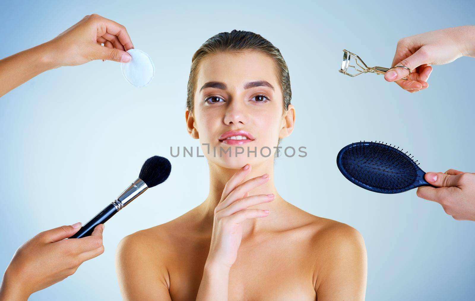 Studio portrait of a beautiful young woman with an assortment of beauty tools around her against a blue background.