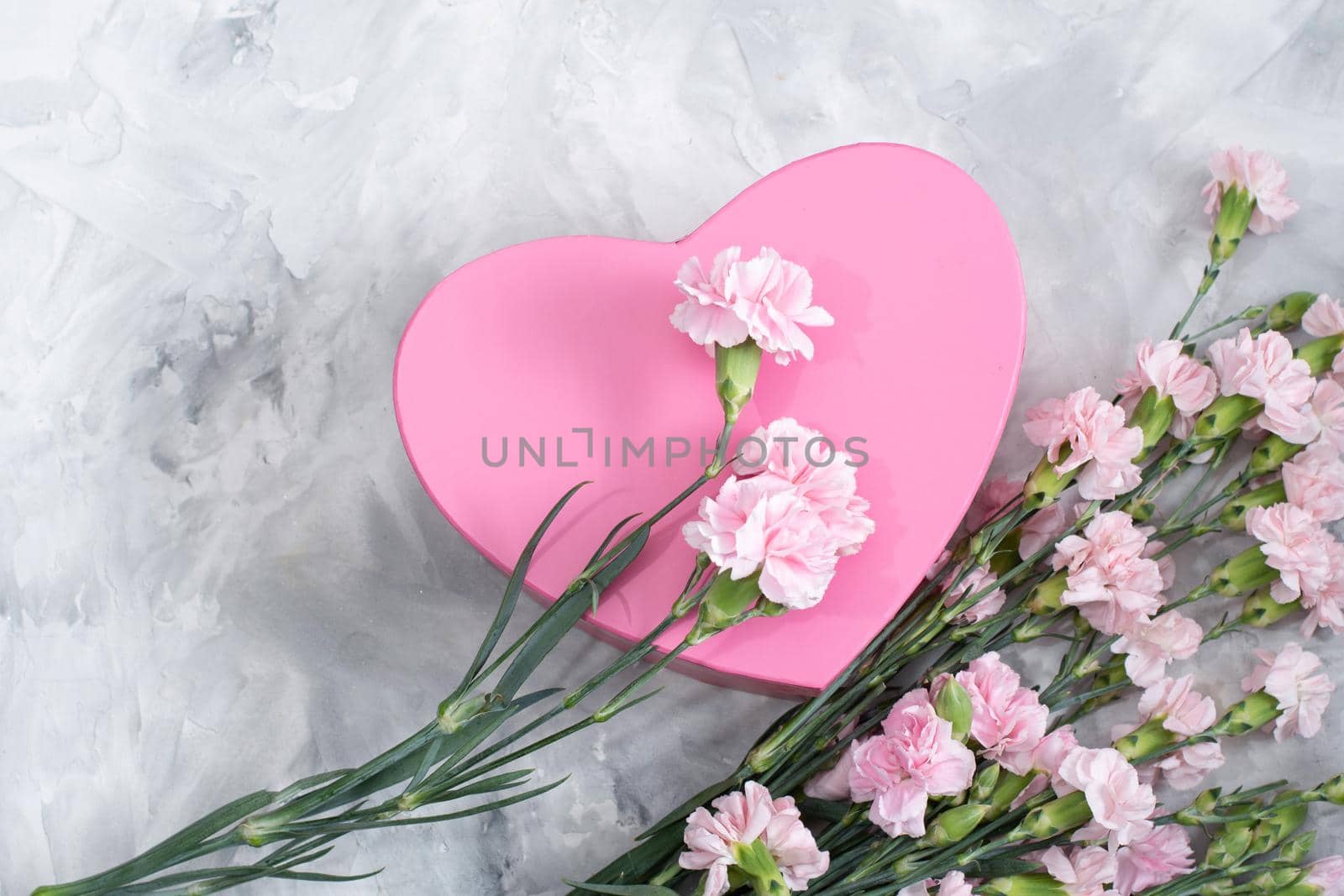 pink carnations and a heart-shaped box on a light gray cement background, a gift for mother's day, valentine's day. High quality photo