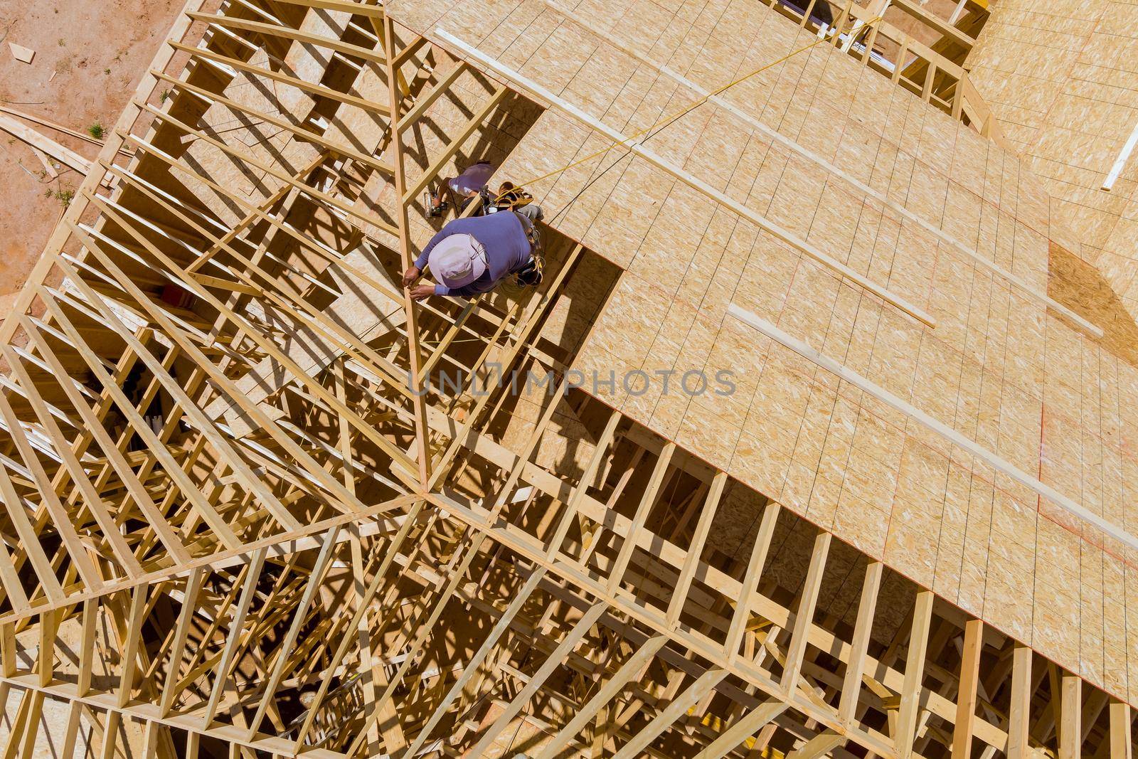 Aerial top view of carpenter with plywood nailing on roof of in unfinished house