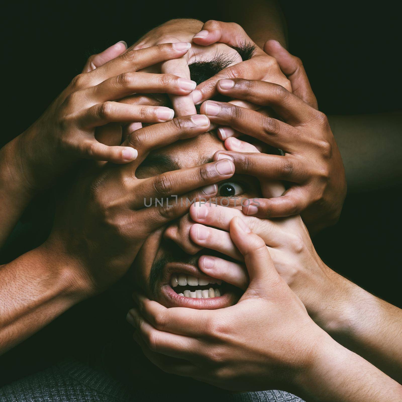 Shot of hands grabbing a young mans face against a dark background.