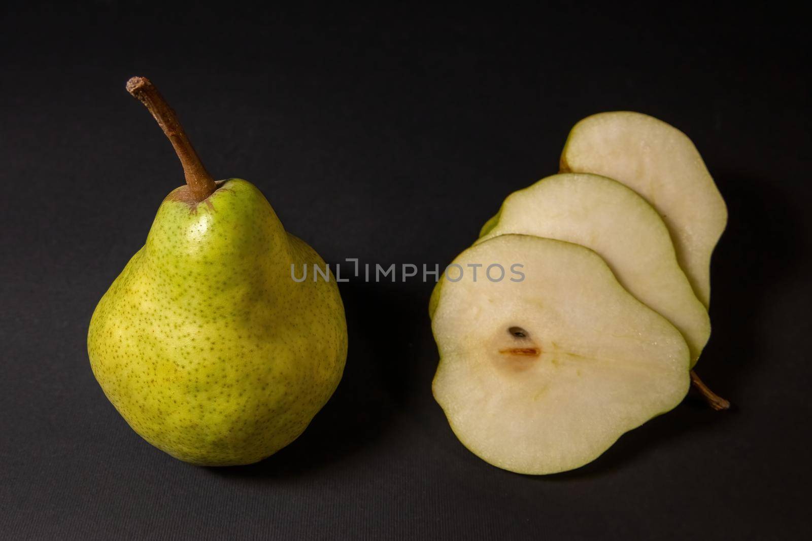 Two ripe green pears on a dark background, late november pear variety. Whole pear and sliced