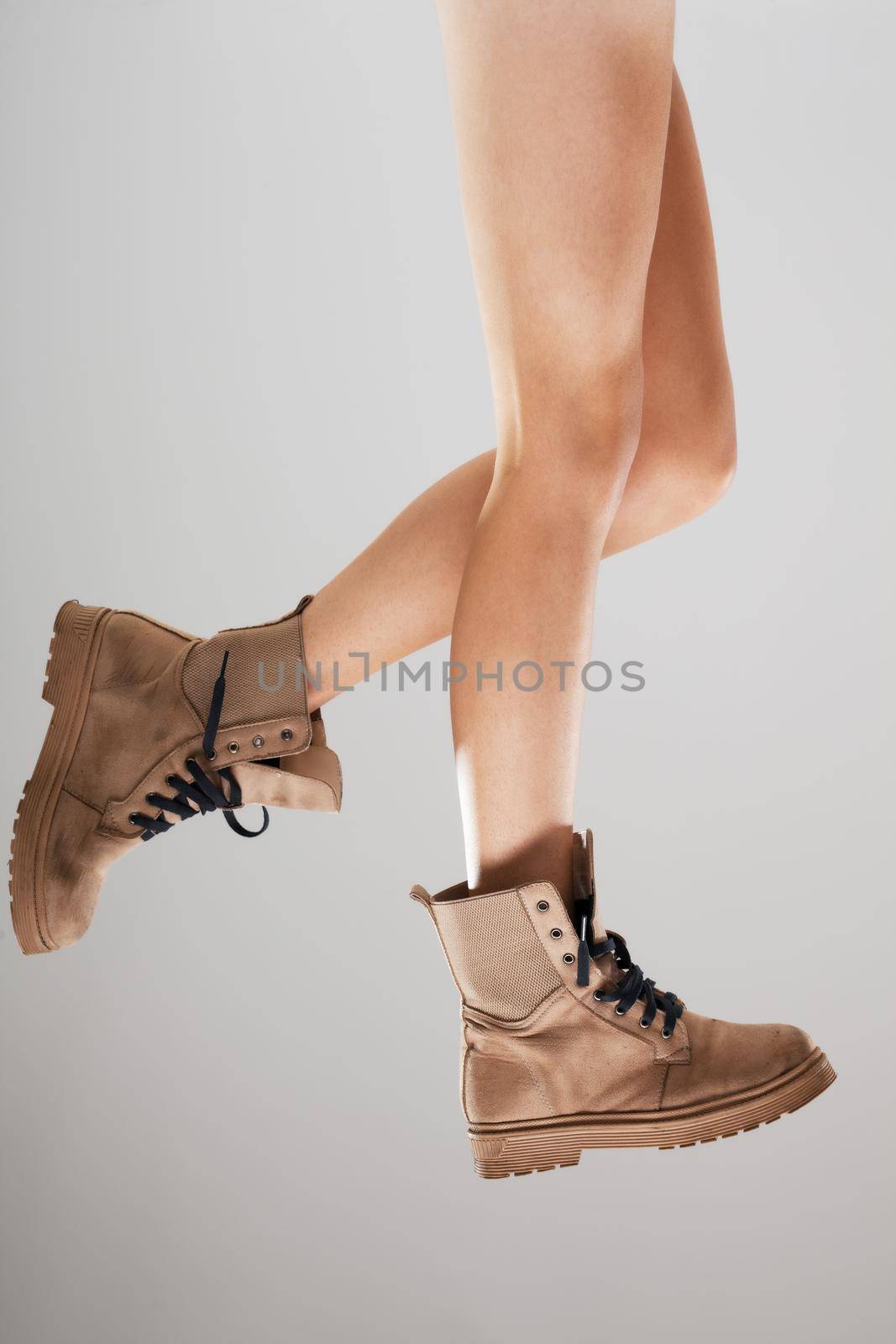 Sexy female legs wearing boots against gray background.