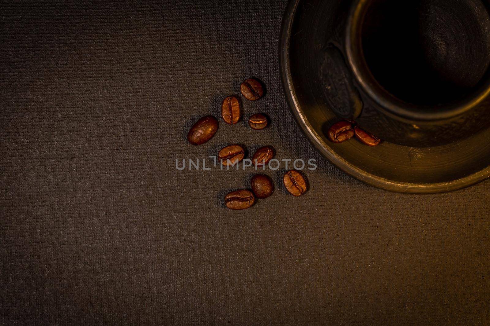 Black clay coffee cup with a saucer and scattered coffee beans near it on dark background