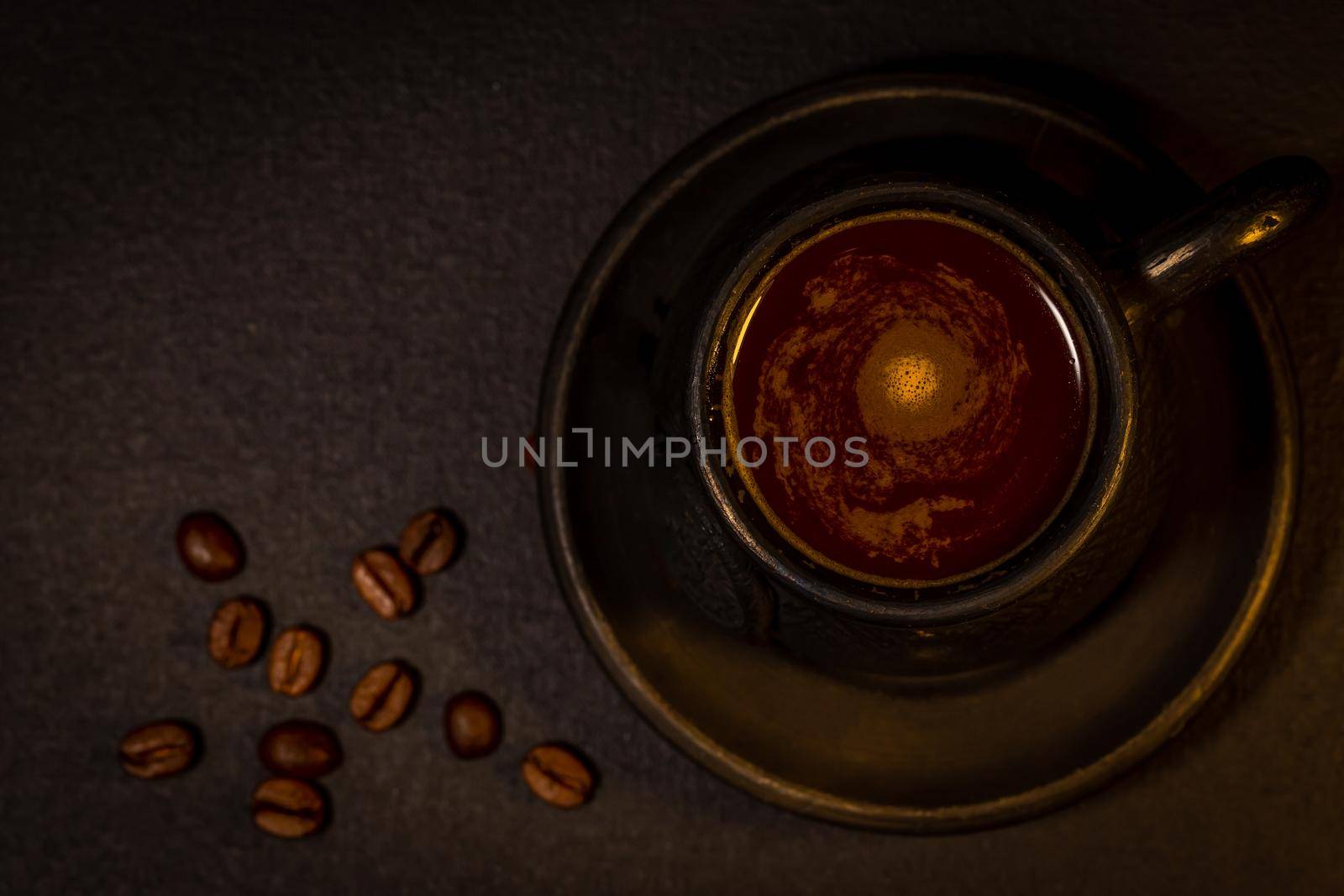 Black clay coffee cup with a saucer and scattered coffee beans near it on dark background