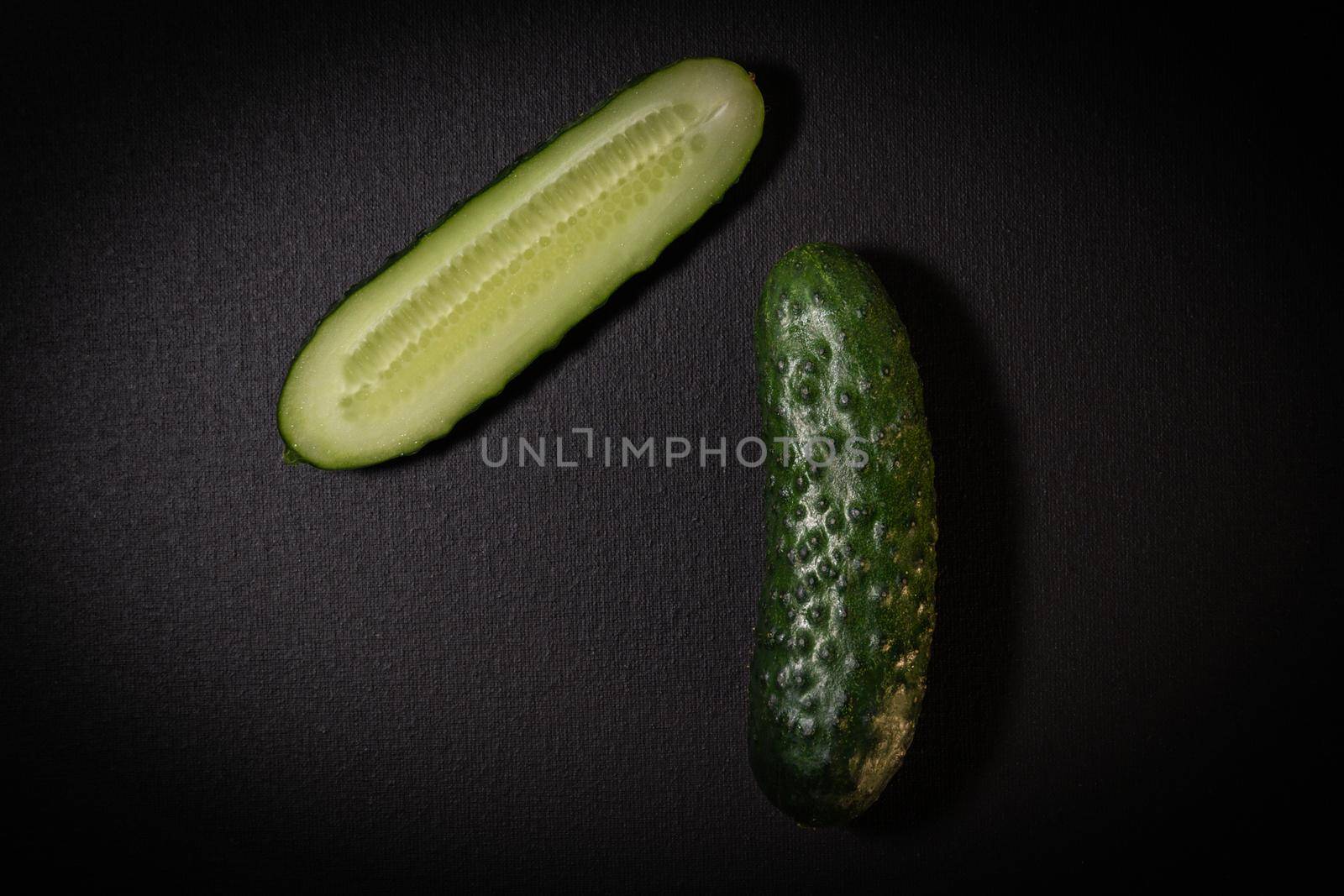 Two green cucumbers on a dark background. Whole cucumber and cut in half