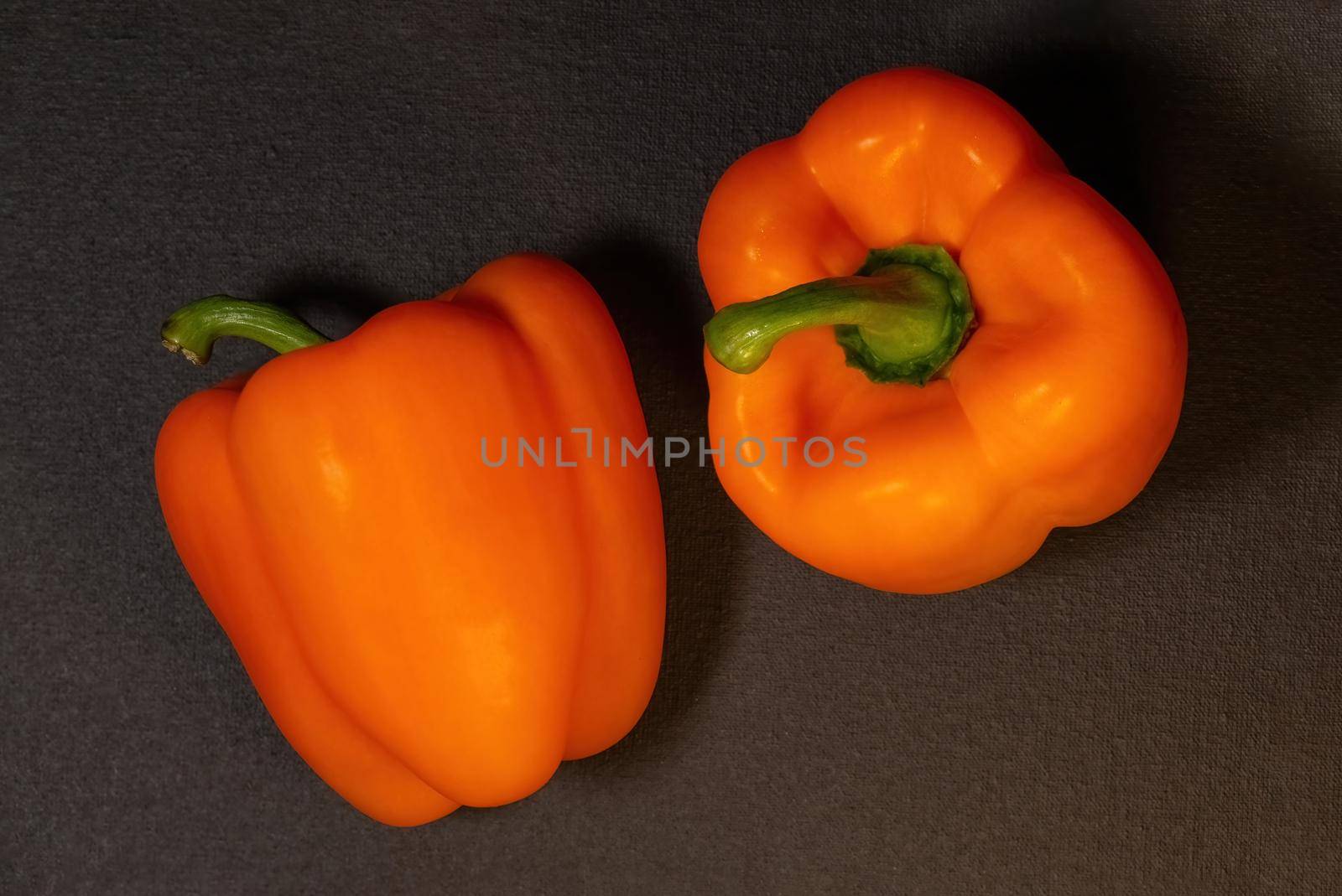Two ripe orange bell peppers on a dark background, whole vegetables