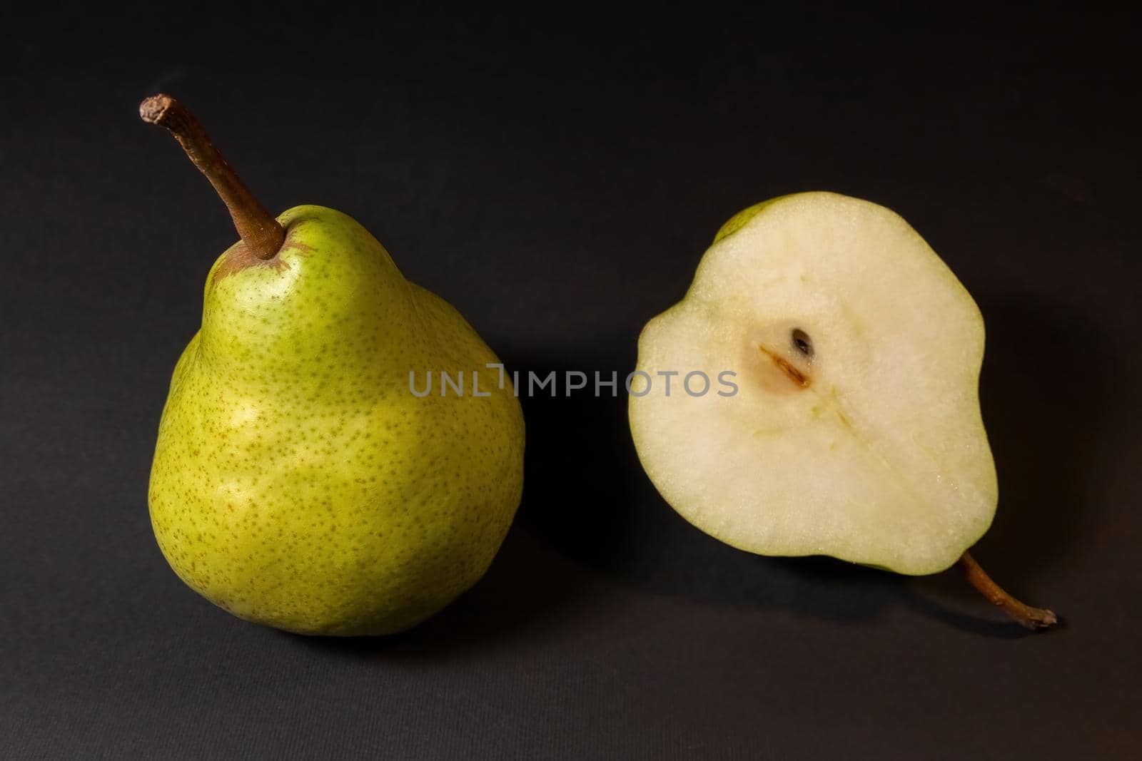 Two ripe green pears on a dark background, late november pear variety. Whole pear and cut in half
