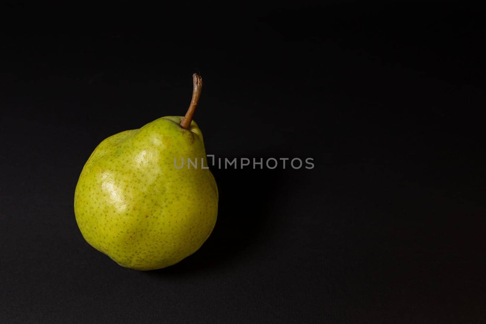 Ripe green pear on a dark background, late november pear variety. Whole fruit
