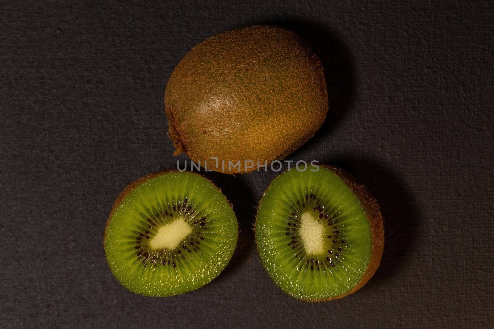 Kiwi fruits on black background. Whole kiwi and cut in half. Top view with copy space, flat lay.