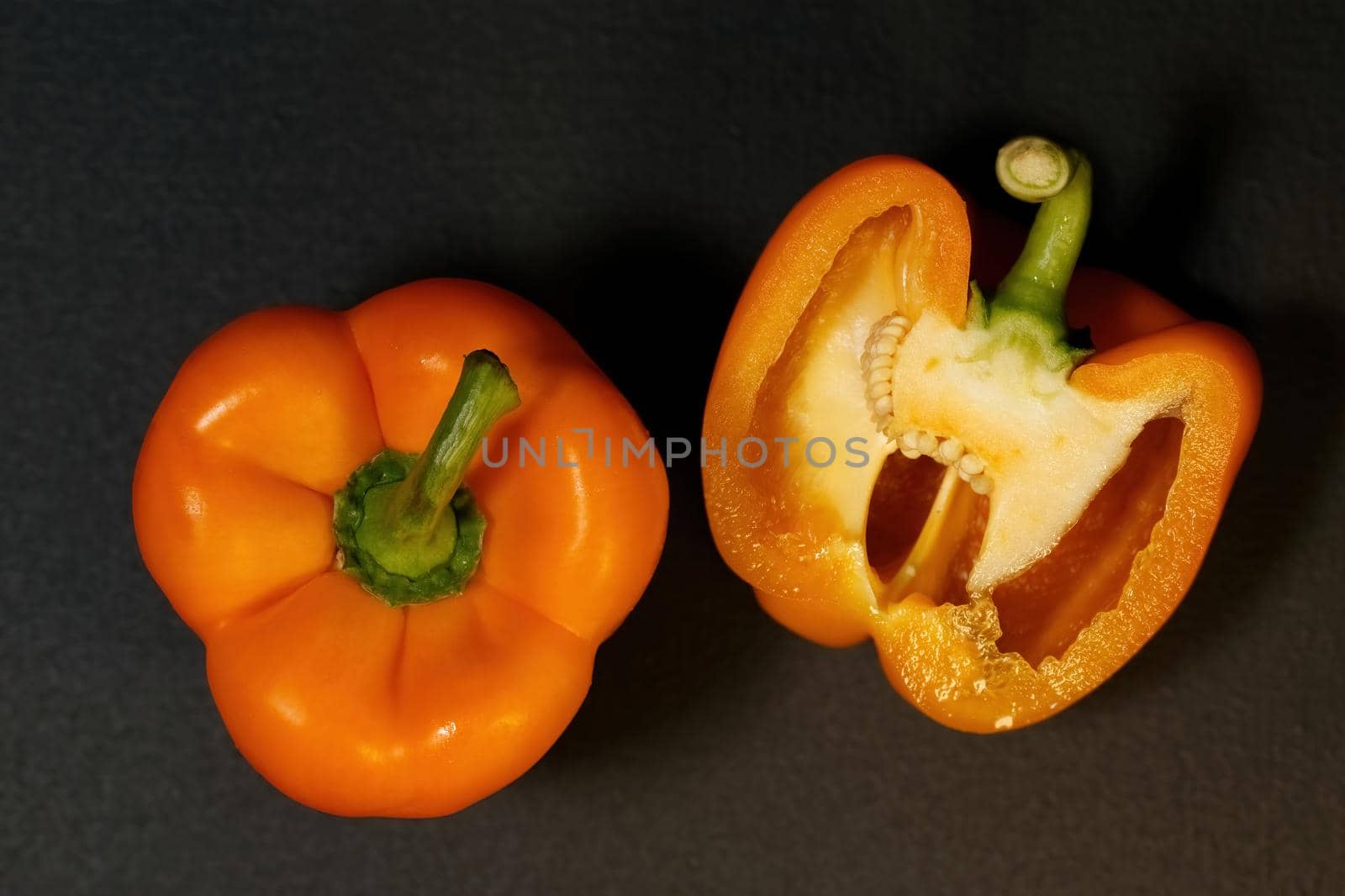 Two ripe orange bell peppers on a dark background, whole bell papper and cut in half