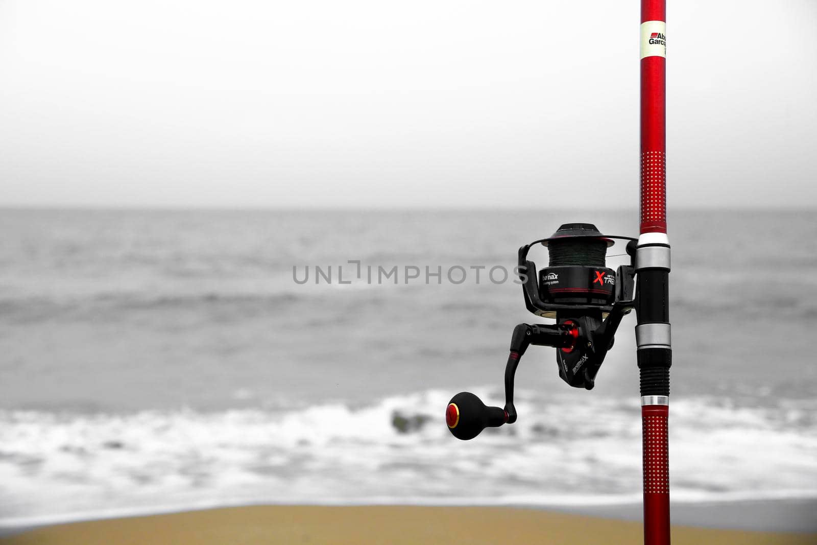 El Pinet, Alicante, Spain- March 30, 2022: Red Fishing rod on the shore on a cloudy day on El Pinet Beach in Alicante