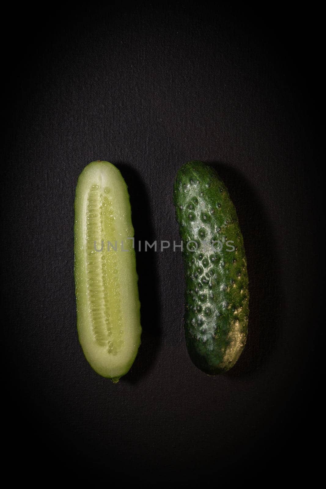 Two green cucumbers on a dark background. Whole cucumber and cut in half