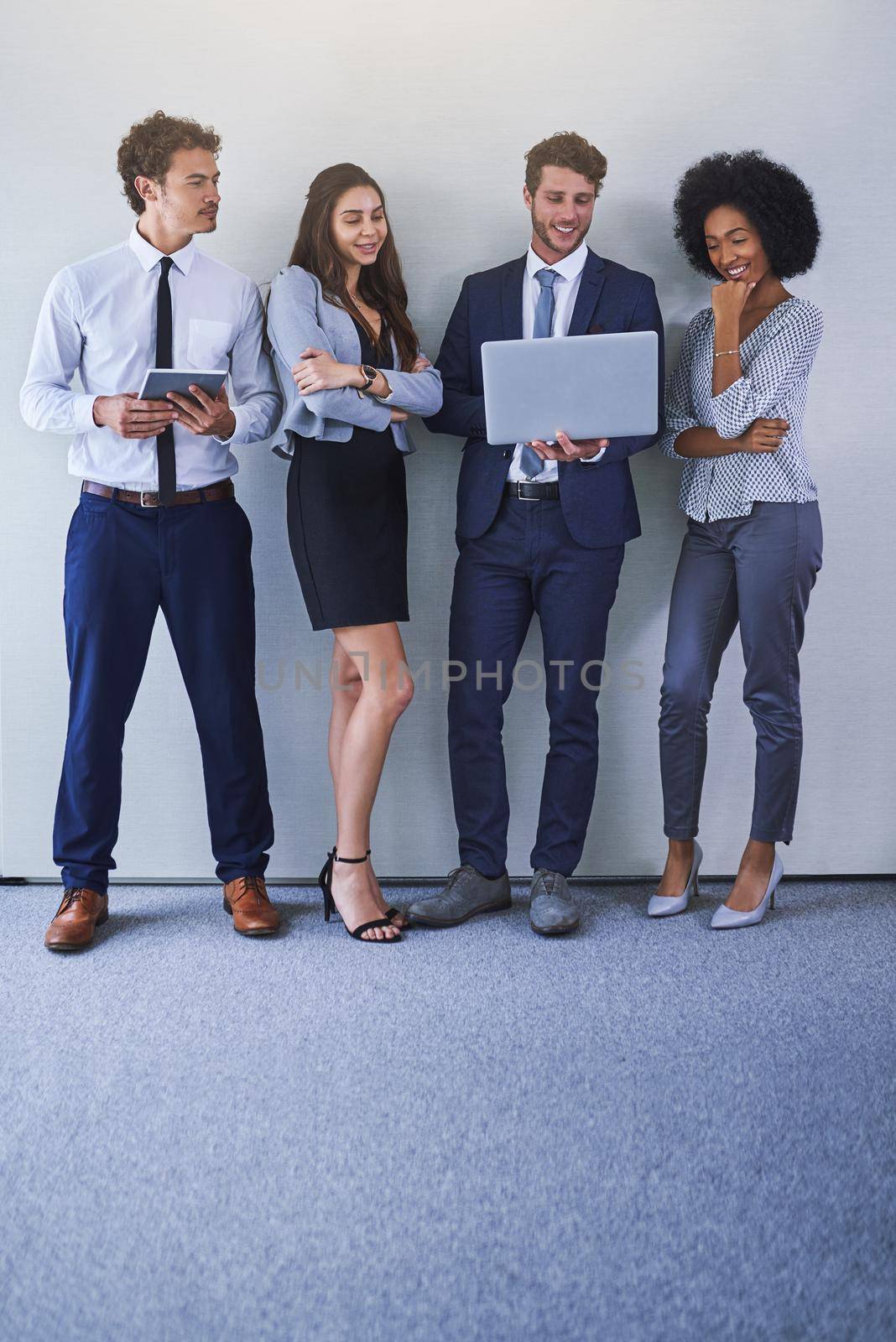 Keeping up with business in the online space. Shot of a diverse group of businesspeople using wireless technology while standing against a grey background. by YuriArcurs