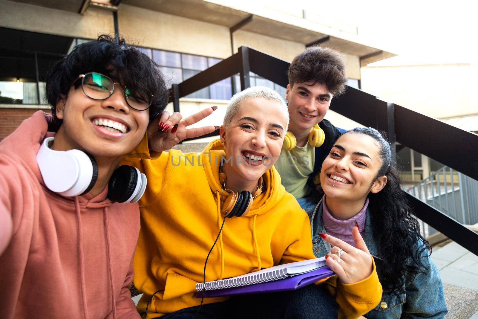 Multiracial group of college friends taking selfie with phone outside university building.Students laughing. having fun. by Hoverstock