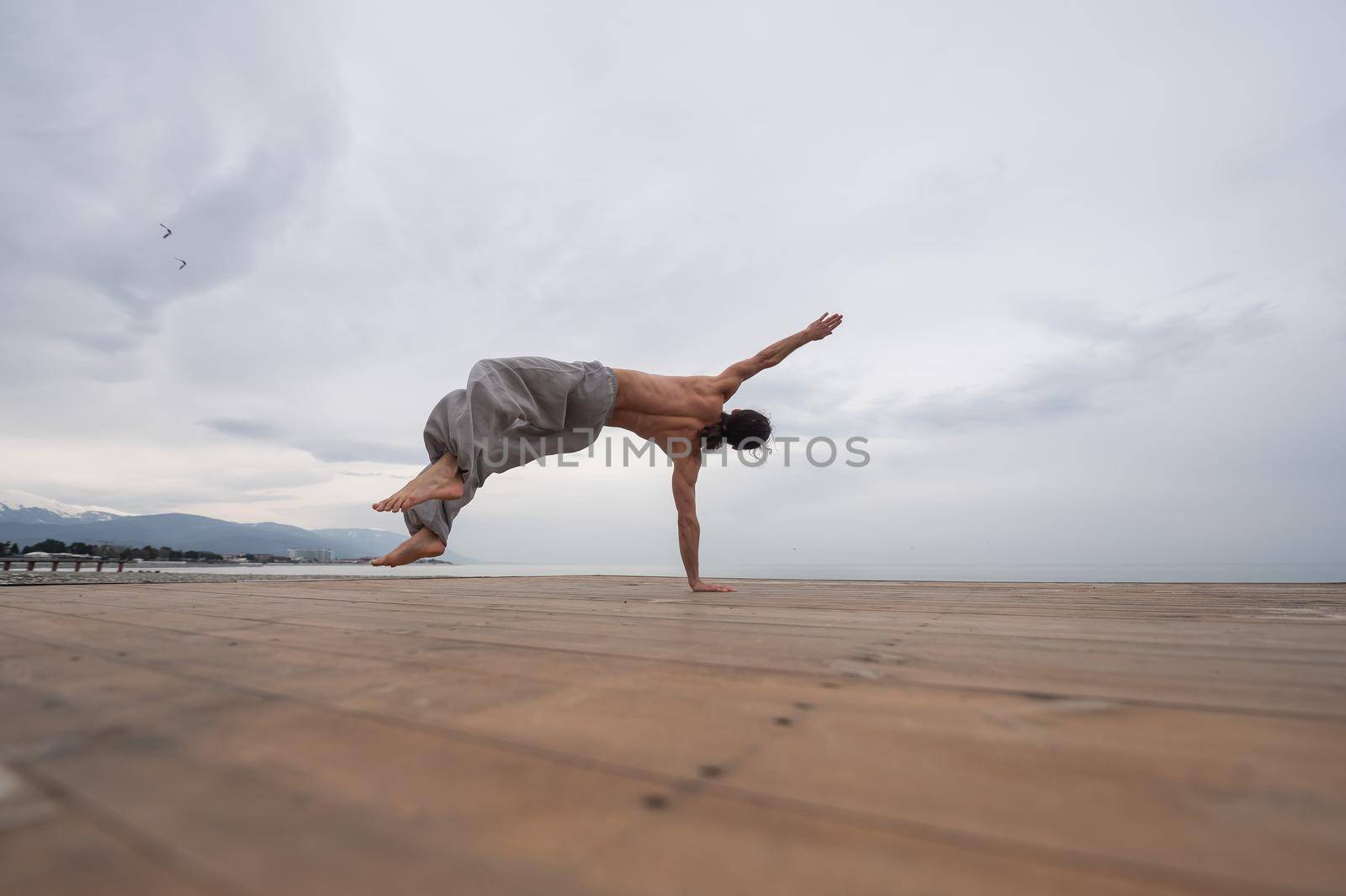 Shirtless caucasian man doing backflip on pebble beach