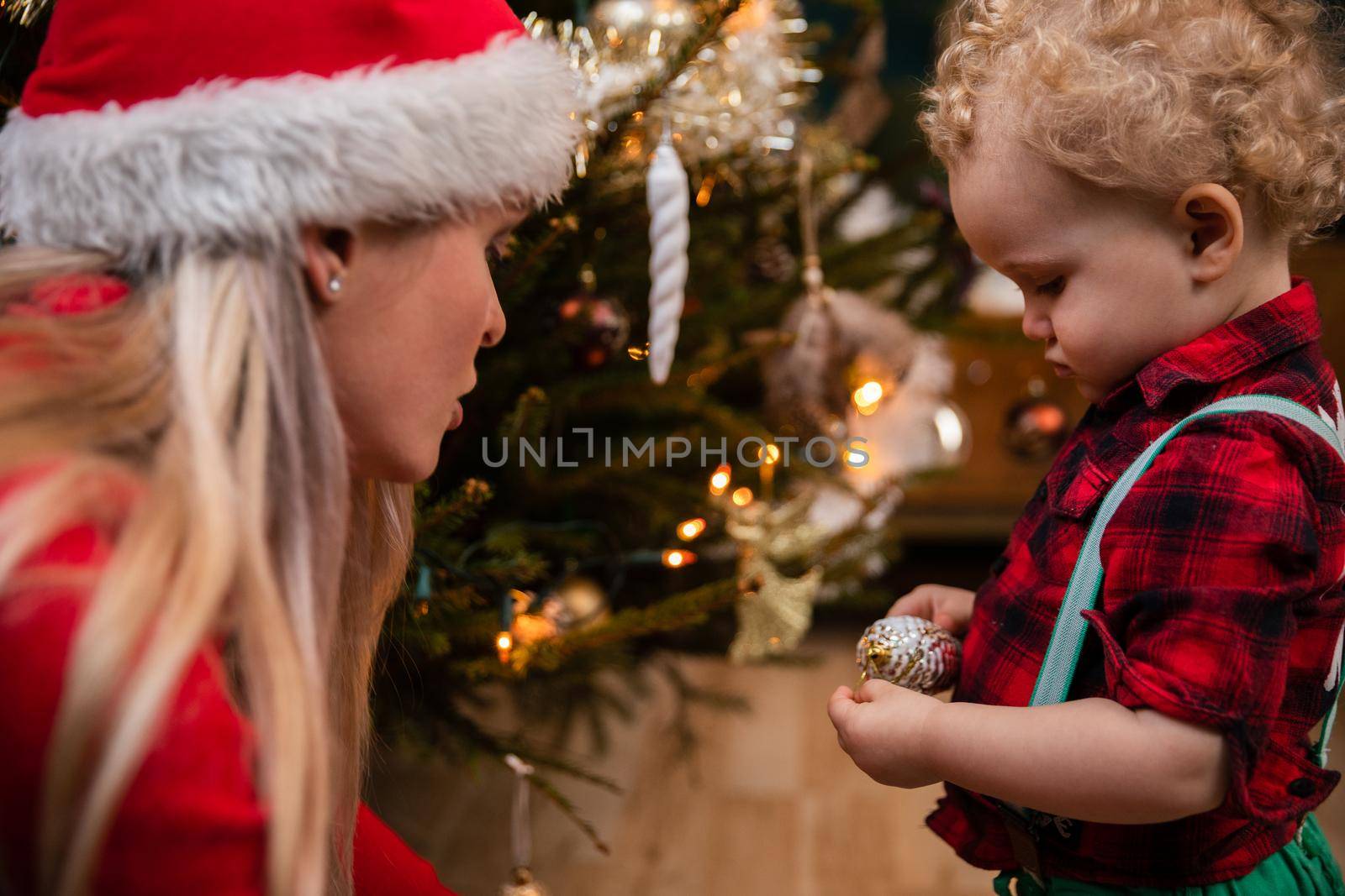 Siblings while decorating a Christmas tree. A two-year-old child with curly blonde hair and a teenage brunette as brother and sister.