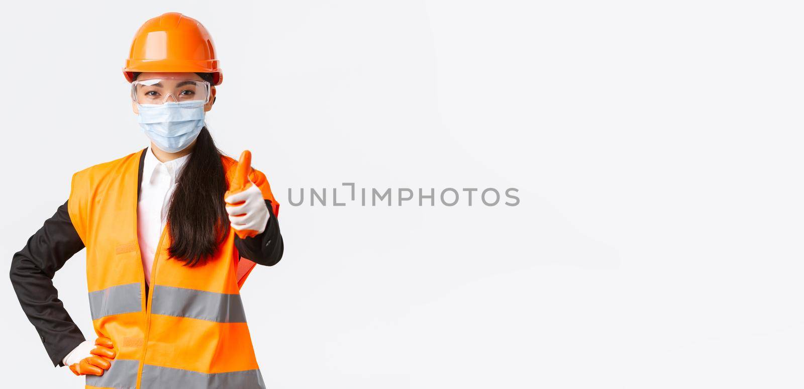 Covid-19 safety protocol at enterpise, construction and preventing virus concept. Confident asian female engineer, architect in face mask and helmet showing thumb-up, guarantee quality of building by Benzoix