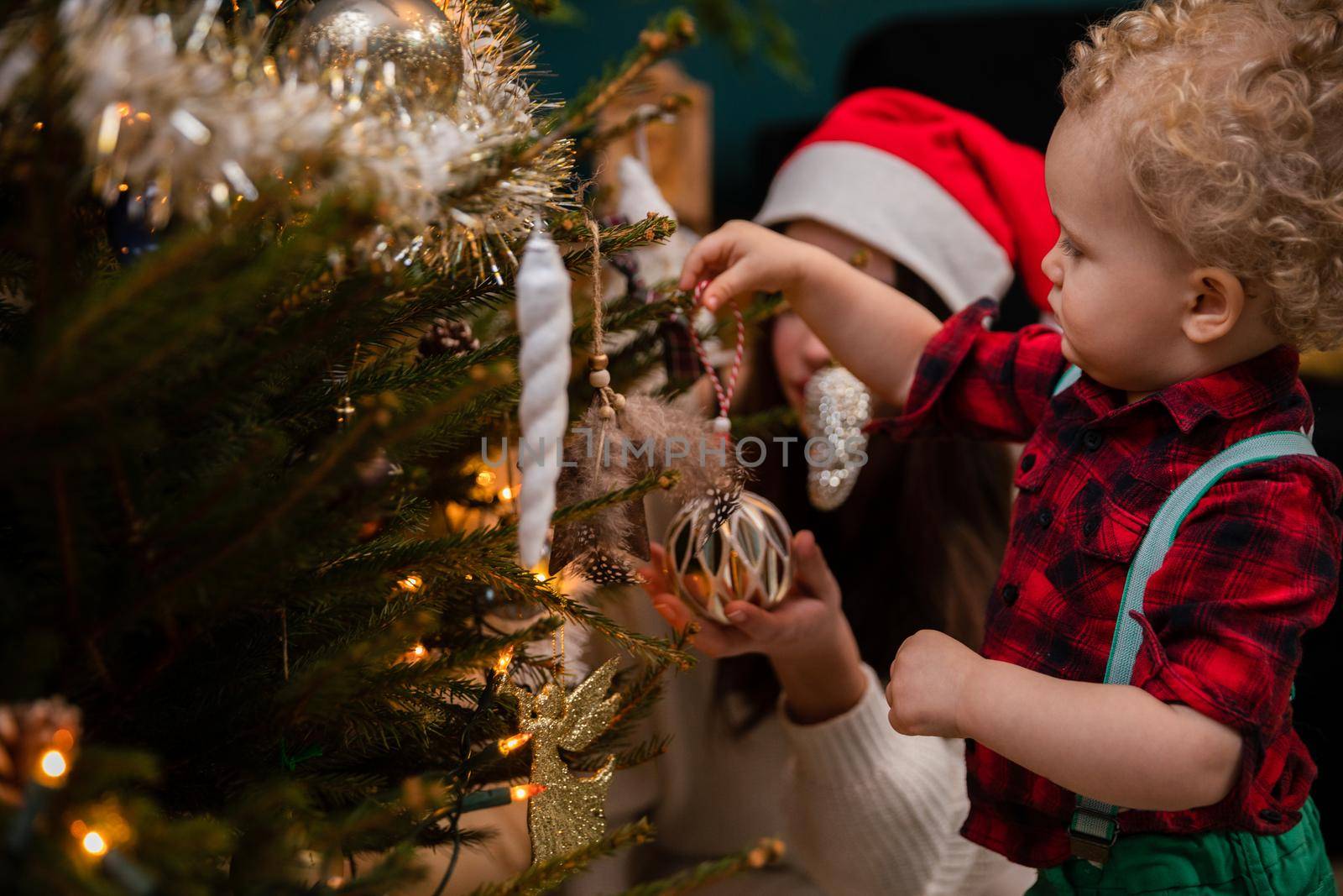 A teenage girl and her brother decorate a Christmas tree for Christmas. A two-year-old child with curly blonde hair.