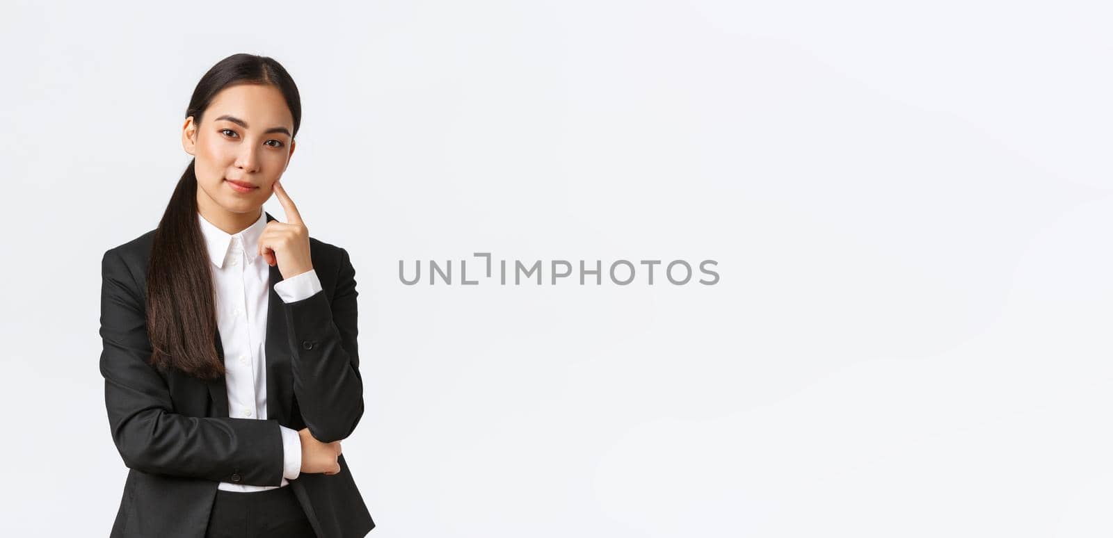 Creative smart asian female manager, saleswoman in suit smiling cunning and looking at camera, have plan, thinking, got excellent idea, standing pleased over white background.