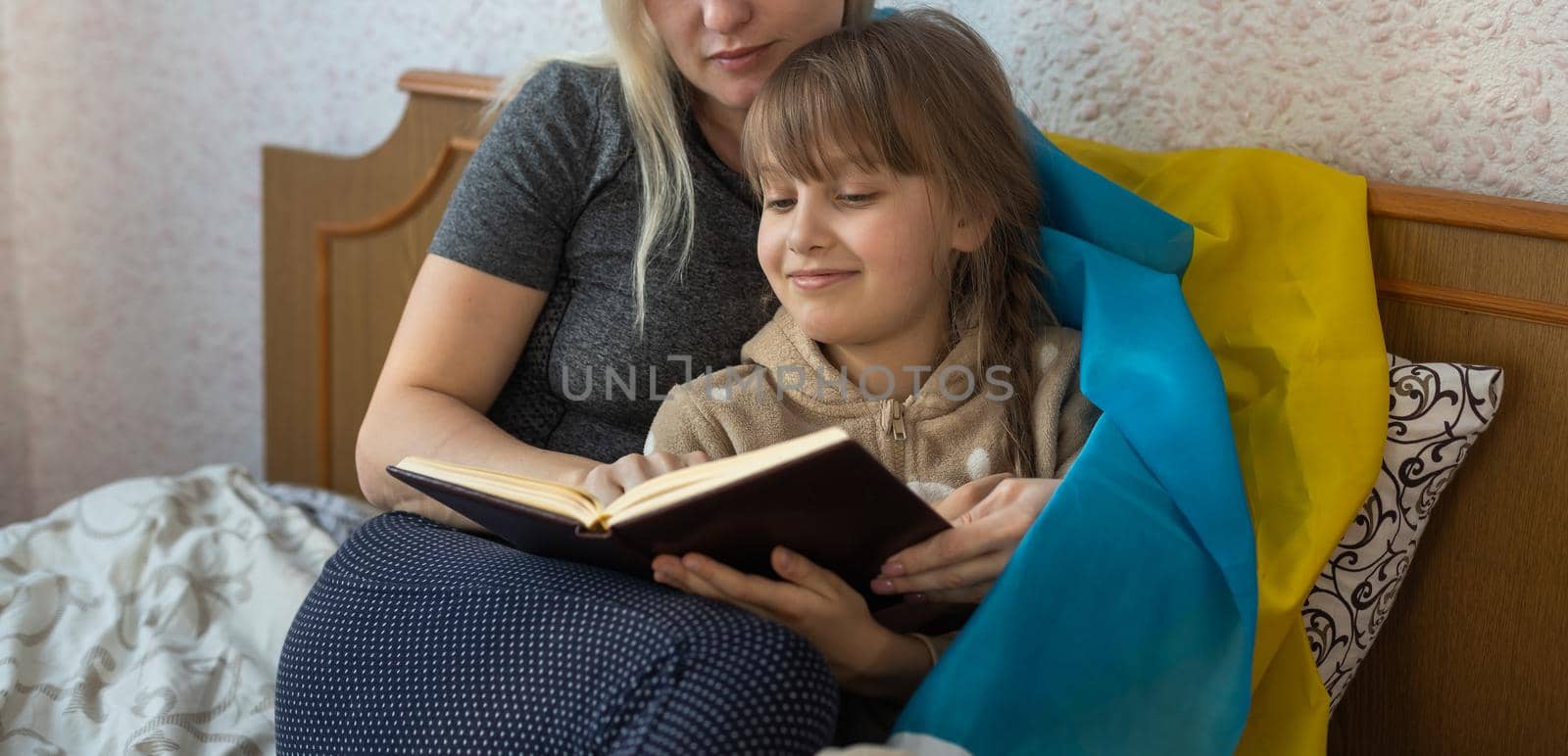 mother and daughter reading a book with the flag of ukraine in bed by Andelov13