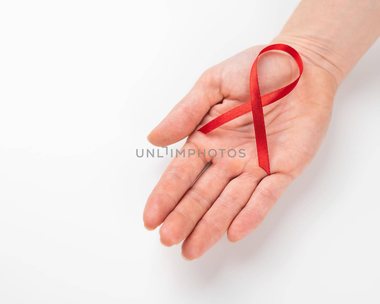 Female palm with a red ribbon on a white background. Symbol of the fight against AIDS