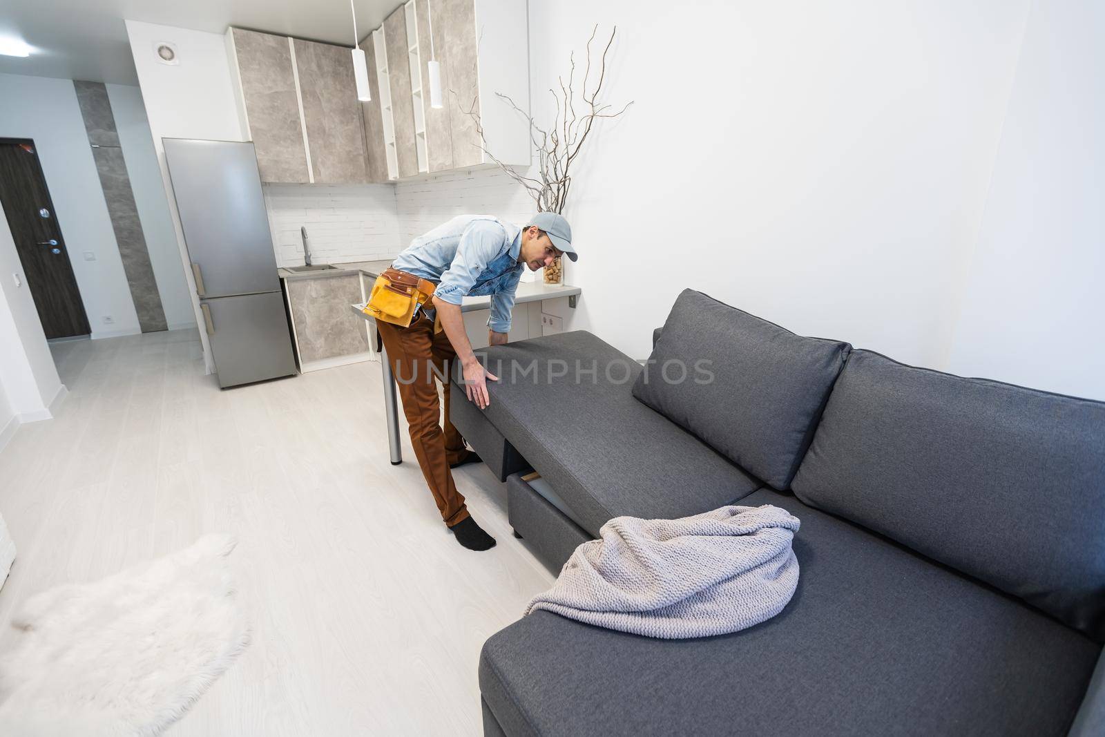 Relocation Concept. Portrait of confident male repairman moving sofa new apartment, replacing furniture at home, caucasian guy placing sofa in cozy studio, side view