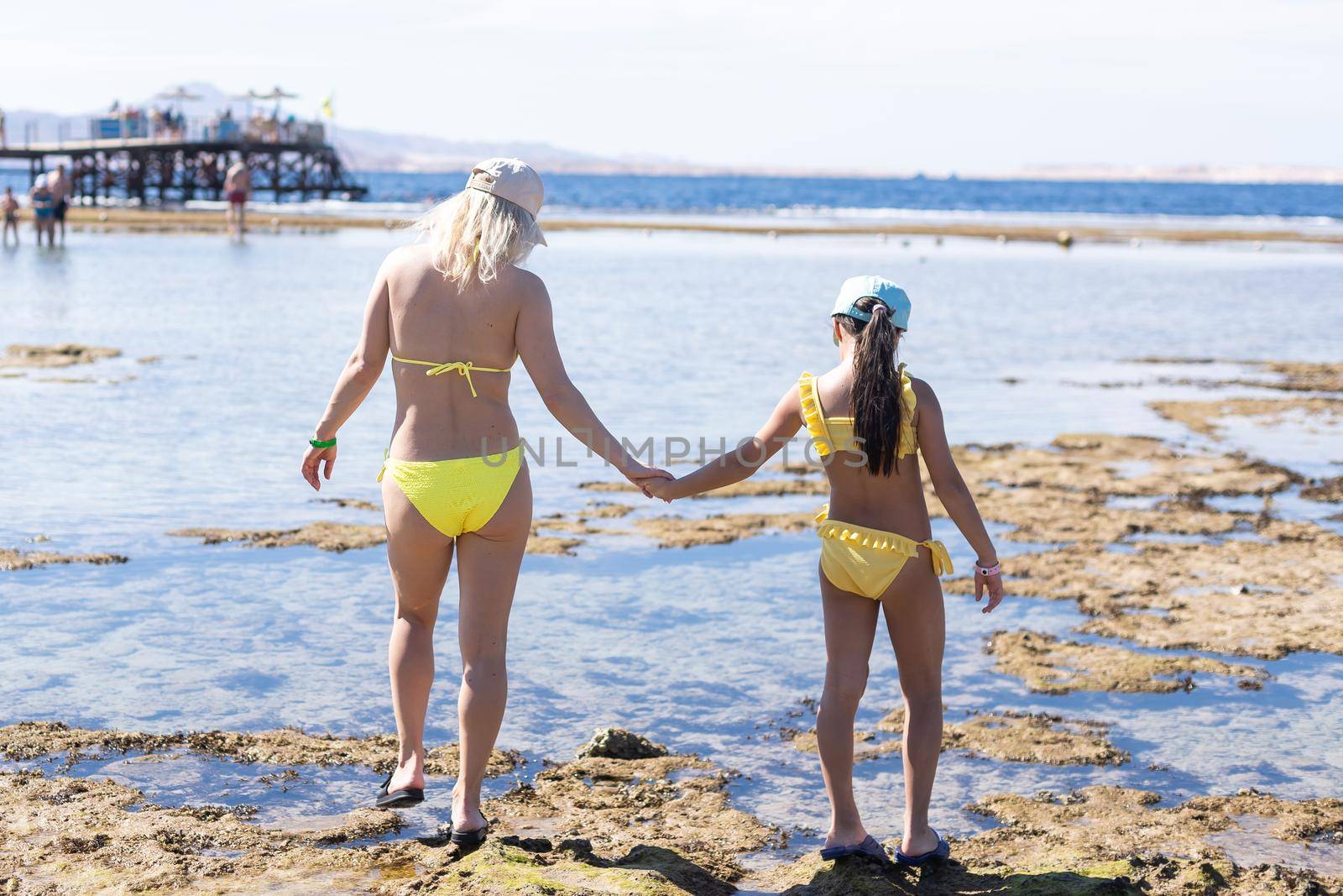 Smiling mother and beautiful daughter having fun on the beach. Portrait of happy woman giving a piggyback ride to cute little girl with copy space.