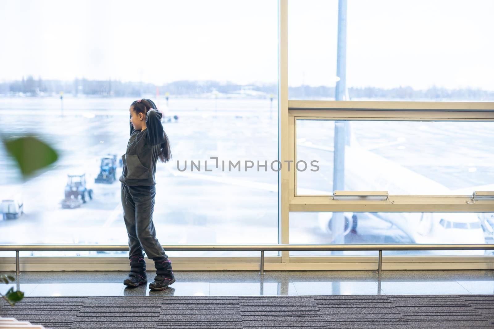 little baby girl waiting boarding to her flight in airport transit hall and looking at airplane parking near departure gate. Travelling by air with child.