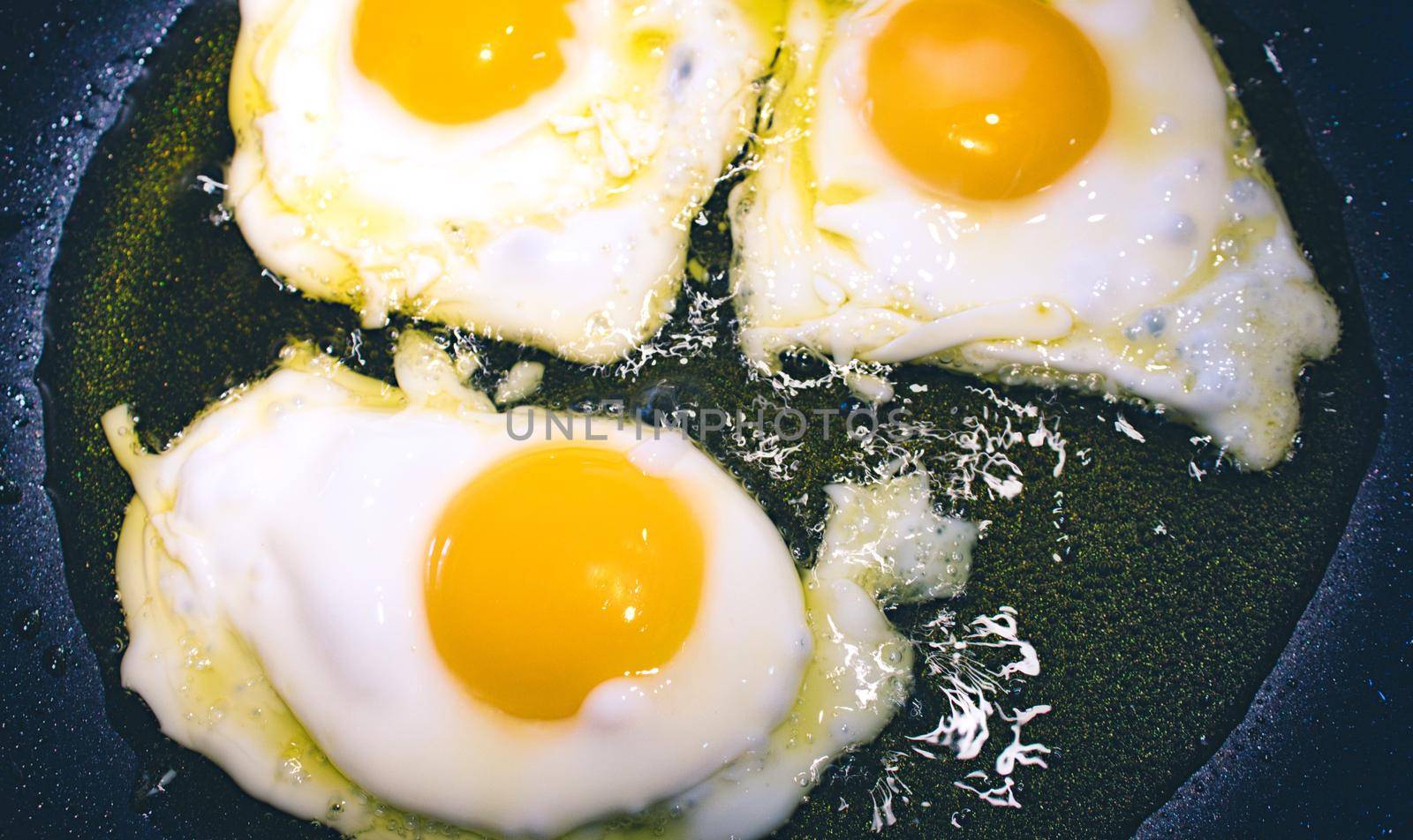 3 fried eggs frying in a pan with olive oil