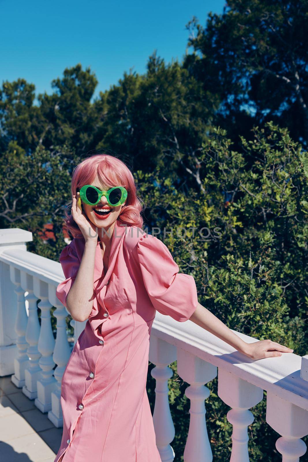 cheerful woman in green glasses pink dress posing outdoors. High quality photo