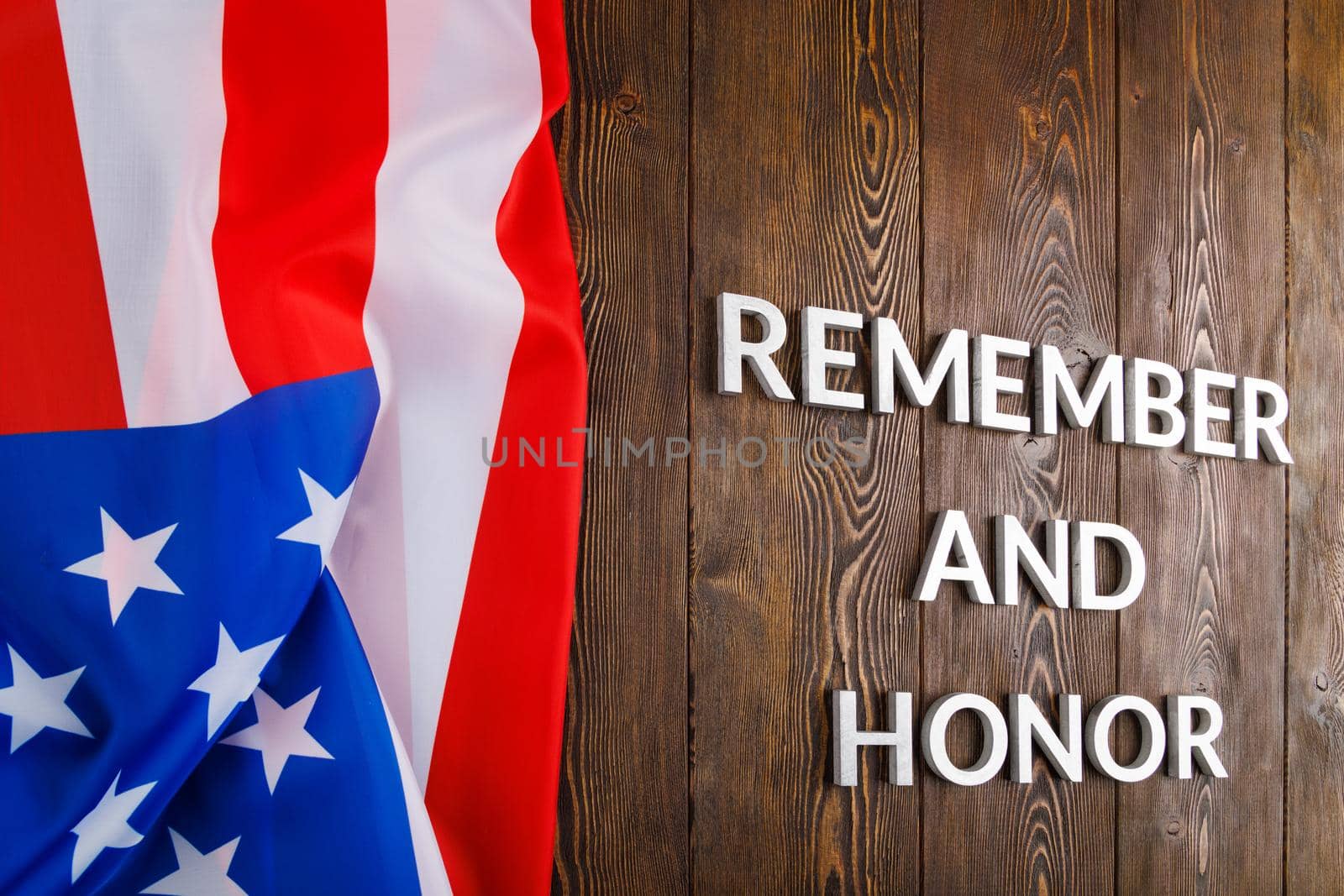 words remember and honor laid with silver metal letters on wooden background with USA flag on the left side in linear perspective