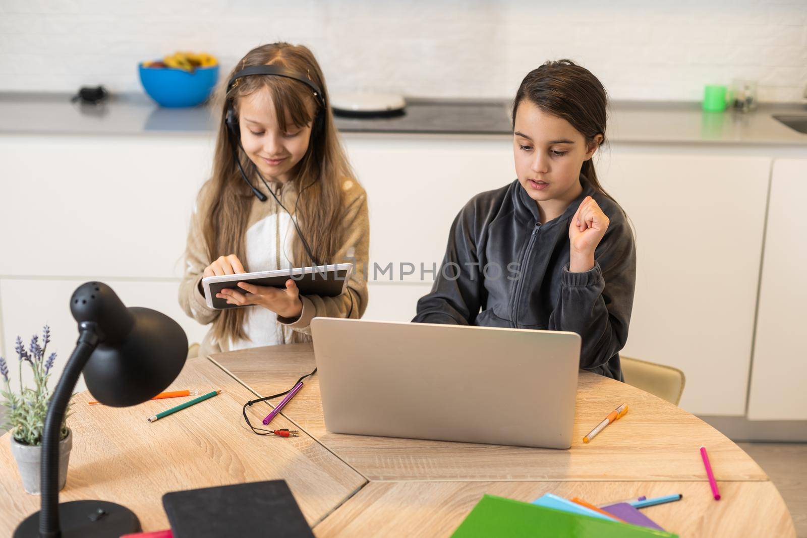 Online training. Two schoolgirl sisters in headphones listen to lessons on laptops. School at home in a pandemic and quarantine