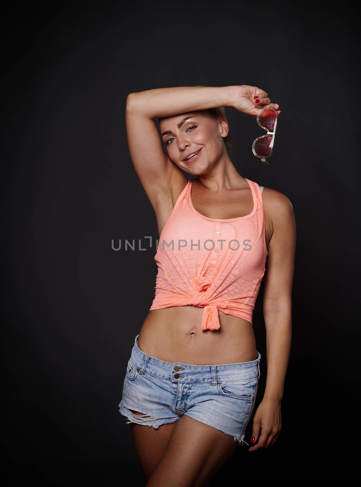 Sexy stunning attractive sporty woman with beautiful muscular body and flat belly, tanned skin, posing over black background with copy space. Sport, summer, motivation concept