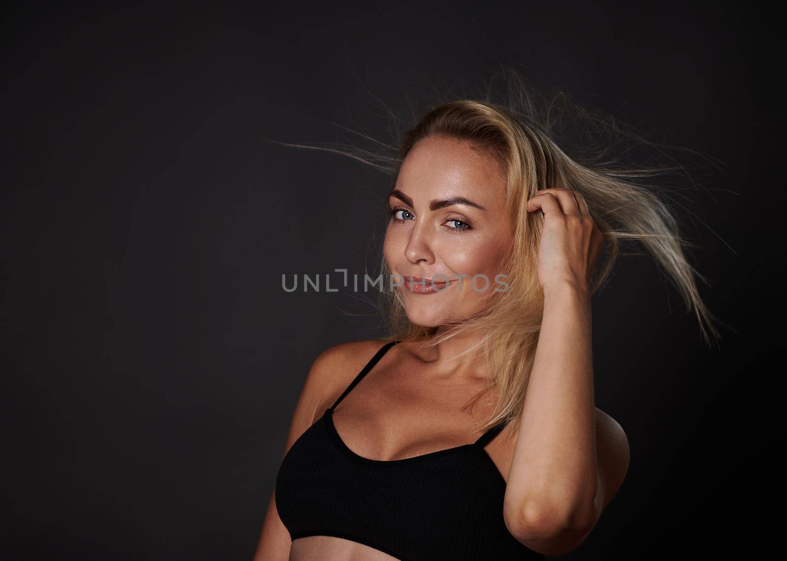 Confident smiling beautiful fitness young Caucasian woman with a healthy toned body, clean glowing tanned skin posing in a black bra against colored background with copy ad space by artgf