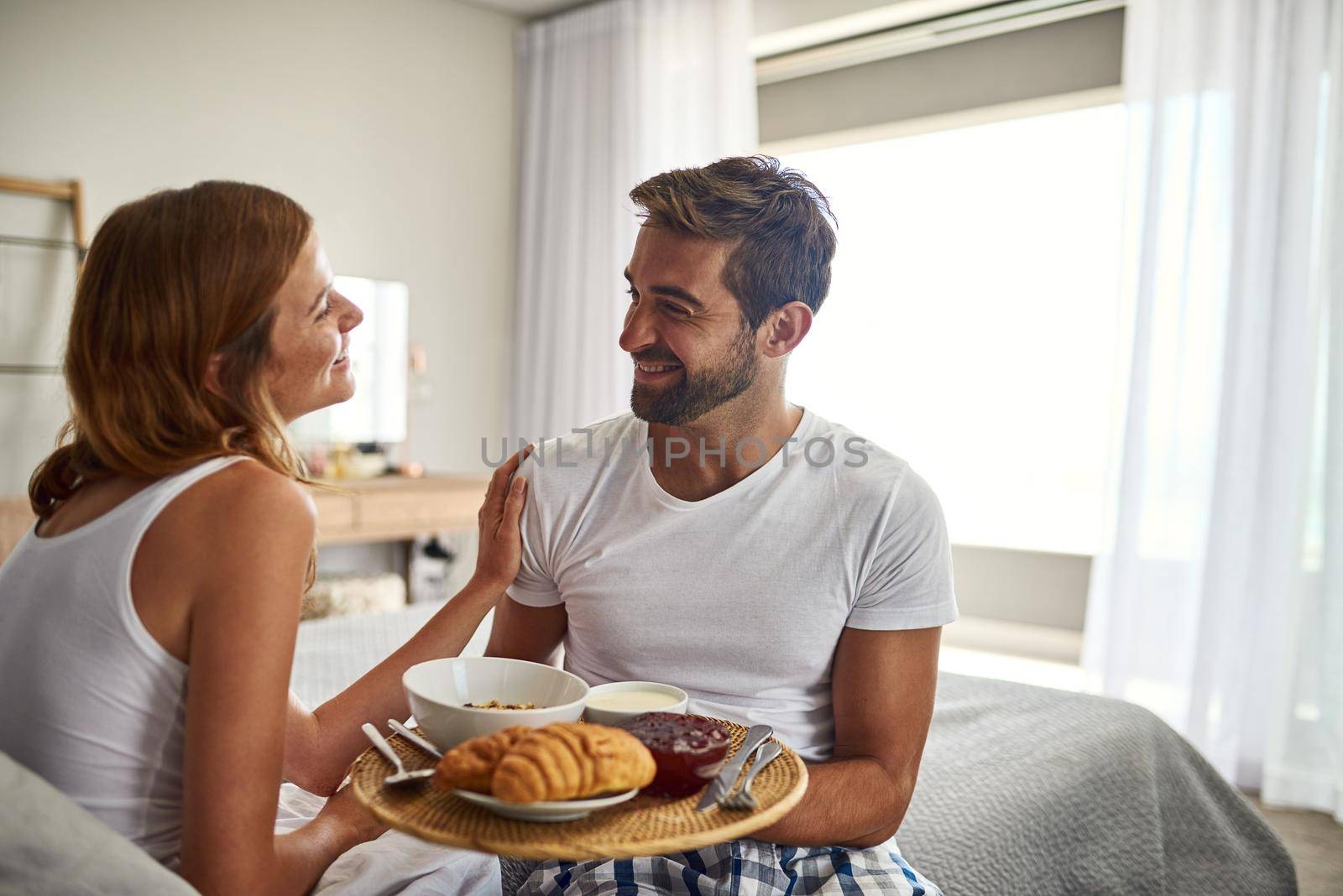 Romance is, breakfast in bed. Shot of a happy young couple enjoying breakfast in bed together at home. by YuriArcurs