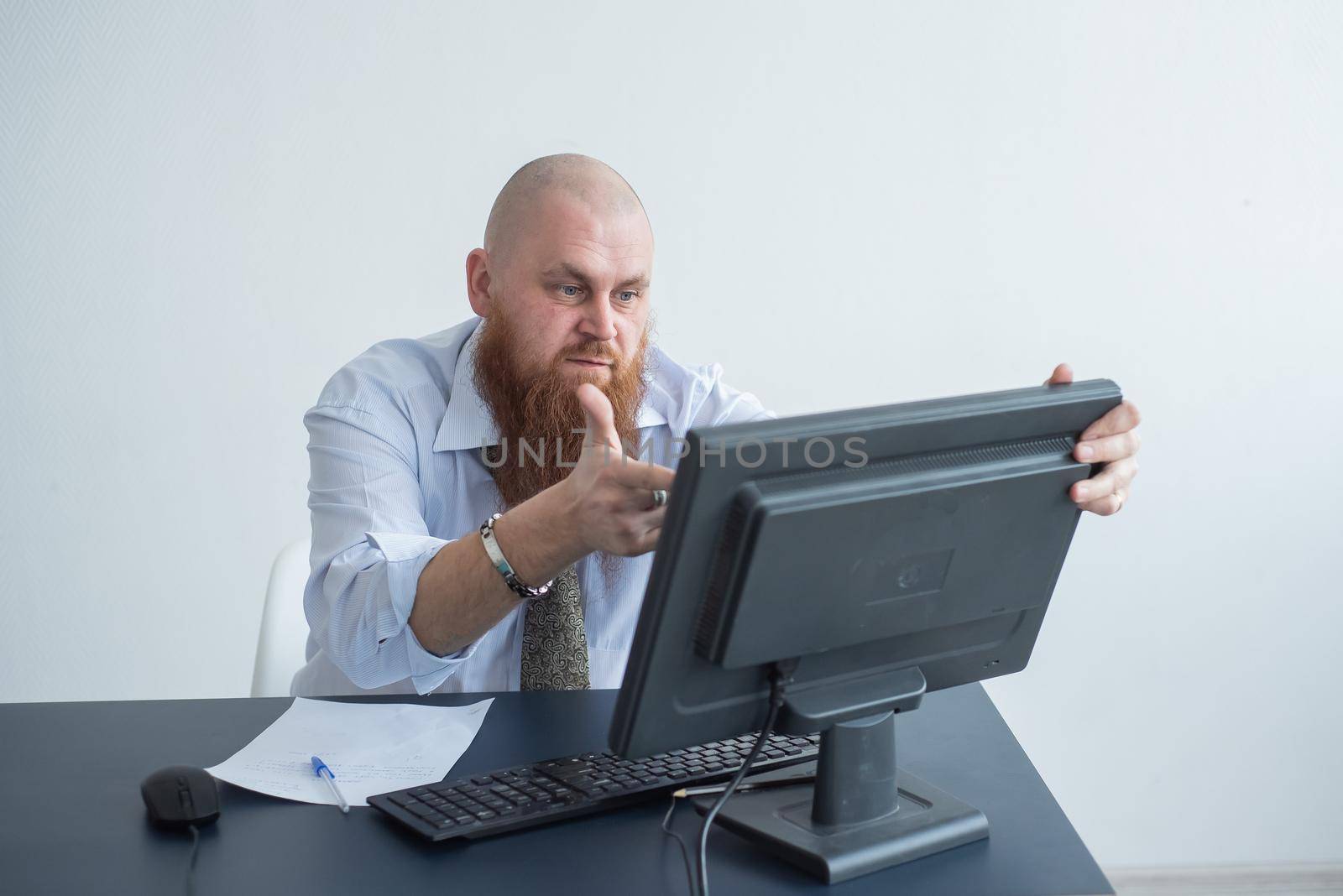 Problems for the office worker. A bald man in a white shirt sits at a desk with a computer and is stressed because of failure. A nervous breakdown