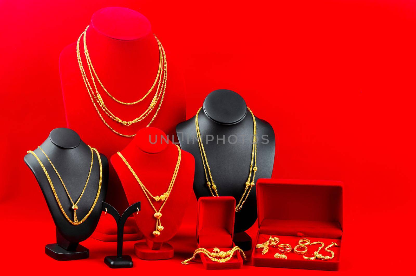Accessory and gold jewelry necklace display stand with gold necklace on red Velvet fabric.